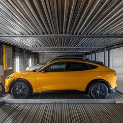La imagen muestra un coche sobre una plataforma dentro de un sistema de estacionamiento automatizado en un moderno garaje subterráneo.