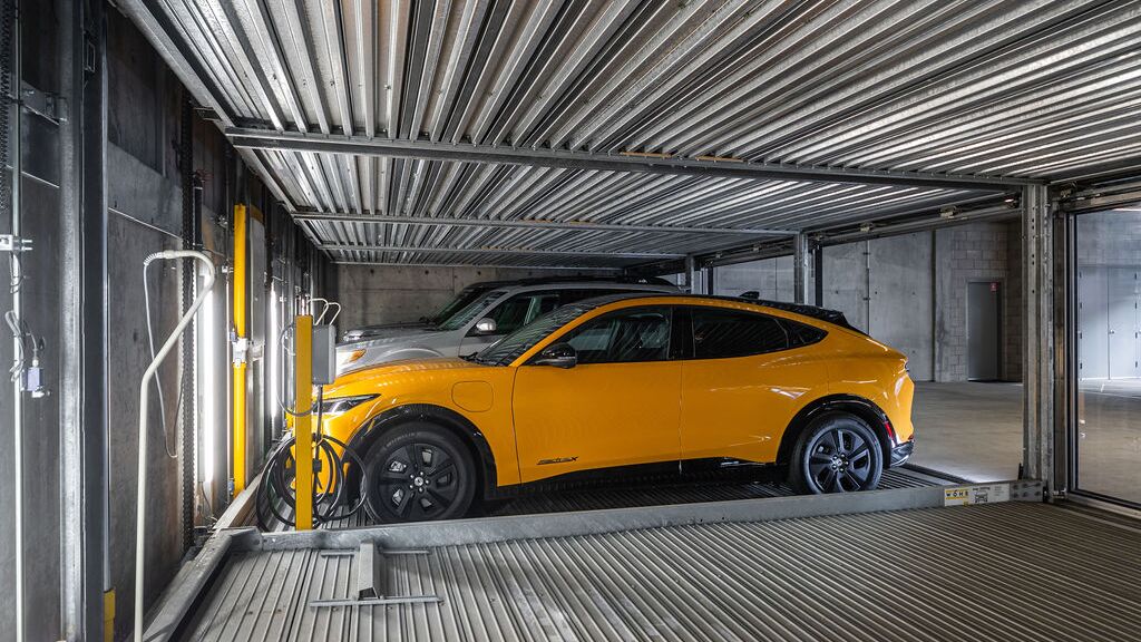 La imagen muestra un coche sobre una plataforma dentro de un sistema de estacionamiento automatizado en un moderno garaje subterráneo.