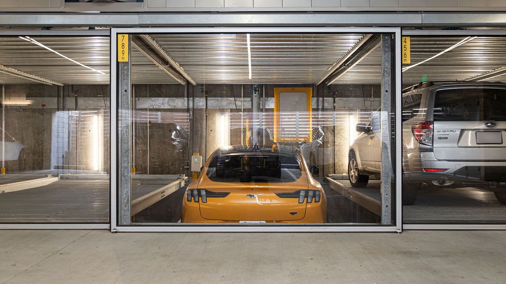La imagen muestra un coche deportivo amarillo en un sistema de estacionamiento dentro de un moderno garaje subterráneo.