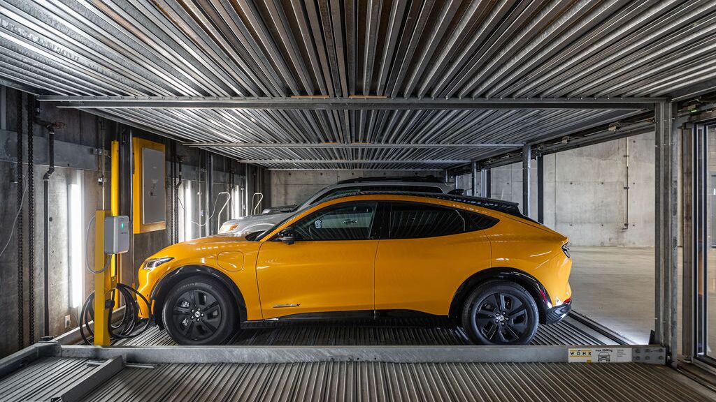 La imagen muestra un coche sobre una plataforma dentro de un sistema de estacionamiento automatizado en un moderno garaje subterráneo.