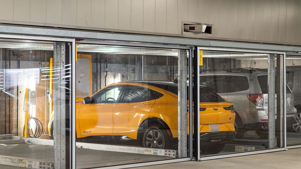 La imagen muestra varios vehículos en plazas acristaladas de un sistema de estacionamiento en un moderno garaje subterráneo.