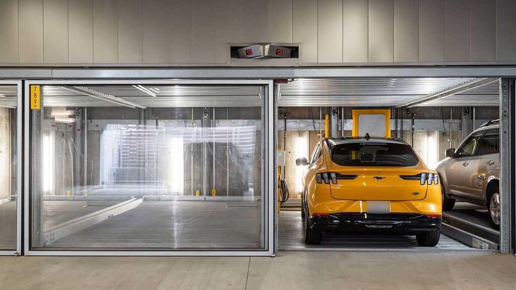 La imagen muestra varios vehículos en plazas acristaladas de un sistema de estacionamiento en un moderno garaje subterráneo.