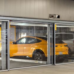 La imagen muestra varios vehículos en plazas acristaladas de un sistema de estacionamiento en un moderno garaje subterráneo.