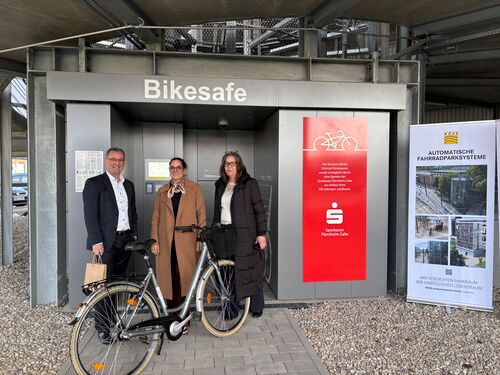 Tres personas con una bicicleta delante de la entrada del sistema automático de aparcamiento para bicicletas