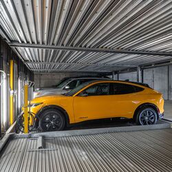 La imagen muestra un coche sobre una plataforma dentro de un sistema de estacionamiento automatizado en un moderno garaje subterráneo.